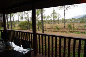 A covered outdoor area with a table and chairs, overlooking a natural landscape with trees and a fenced field. - Le Gite du Koniambo (Voh)