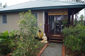 Une maison dotée d’un porche abrité, d’une petite statue et d’un jardin où poussent différentes espèces de plantes.
