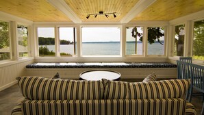 Een kamer met uitzicht op een meer, een gestreept bankje, een ronde tafel en een houten plafond.