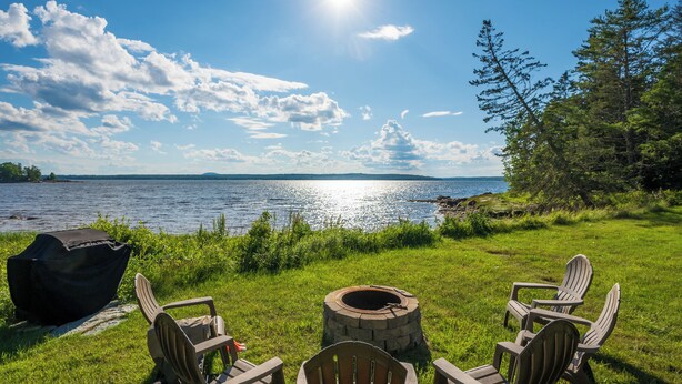 Uitzicht op een meer met Adirondack stoelen, een vuurplaats en een barbecue.