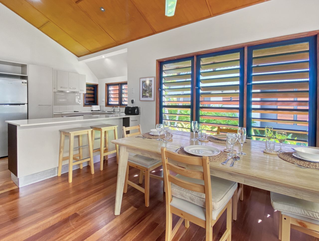 A modern kitchen with white cabinets, a central island, and a dining area with wooden chairs and a table set for four.
