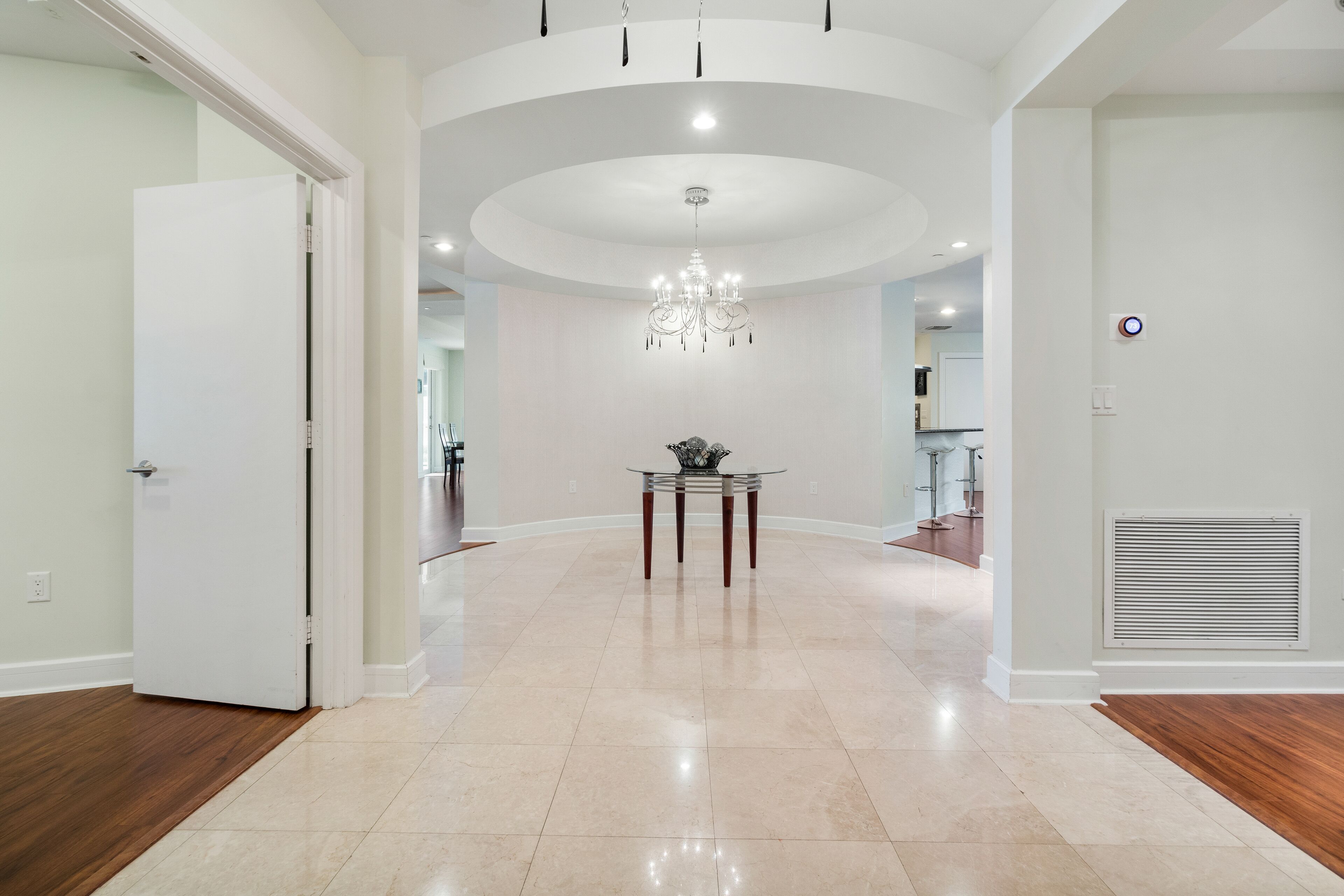 A spacious hallway with a chandelier, a table with a vase, and a vent on the wall.