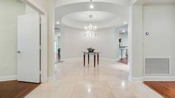 A spacious hallway with a chandelier, a table with a vase, and a vent on the wall.