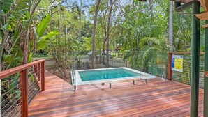 Una terraza de madera con piscina, rodeada de abundante vegetación y un letrero de RCP.