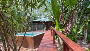 Una terraza de madera que conduce a una piscina con zona vallada, rodeada de vegetación tropical.