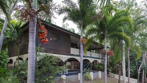 Un edificio de dos pisos con balcón, rodeado de vegetación tropical.
