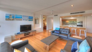 Ein modernes Wohnzimmer mit Fernseher, Sofas, einem Couchtisch und einer Küchenzeile.