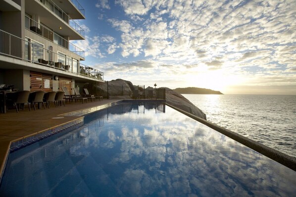 Ein Poolbereich mit Liegestühlen und Blick auf das Meer bei Sonnenuntergang.