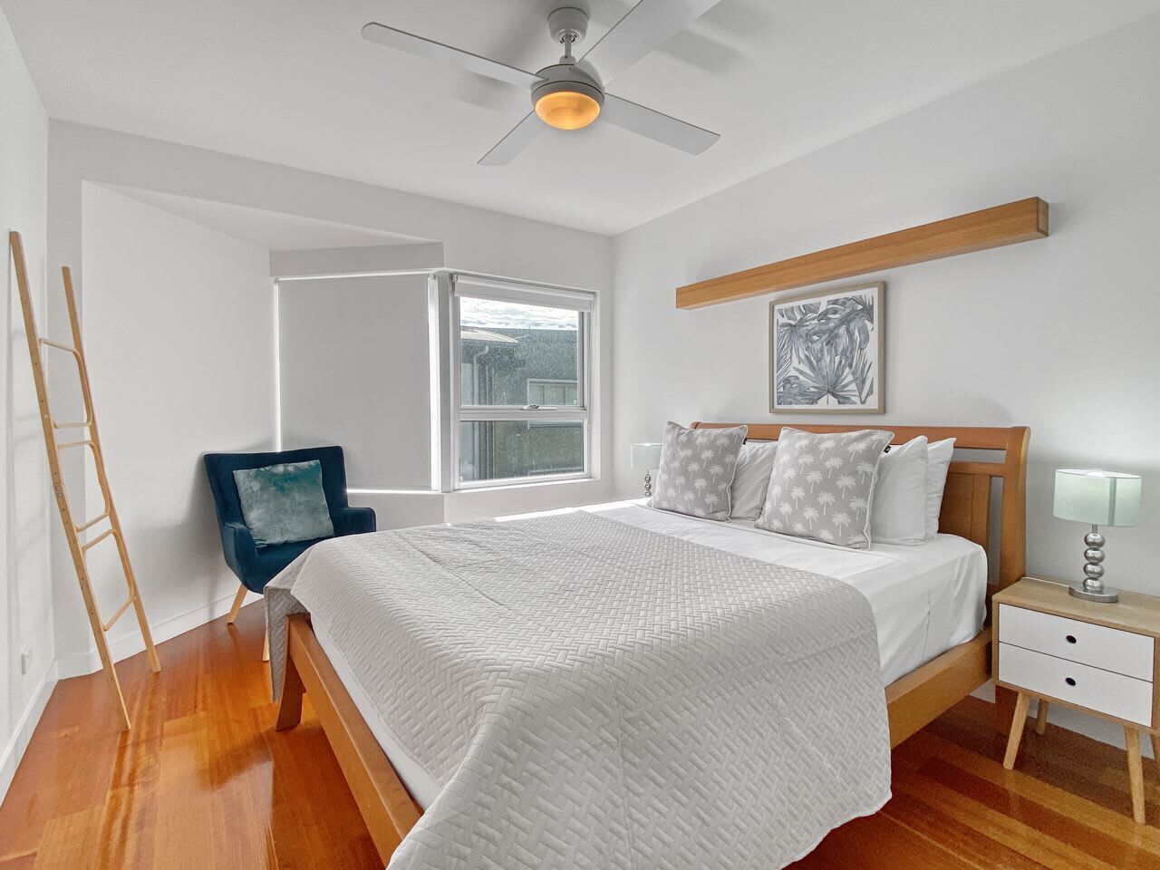 A bedroom with a bed, a nightstand, a chair, a ladder, and a ceiling fan.