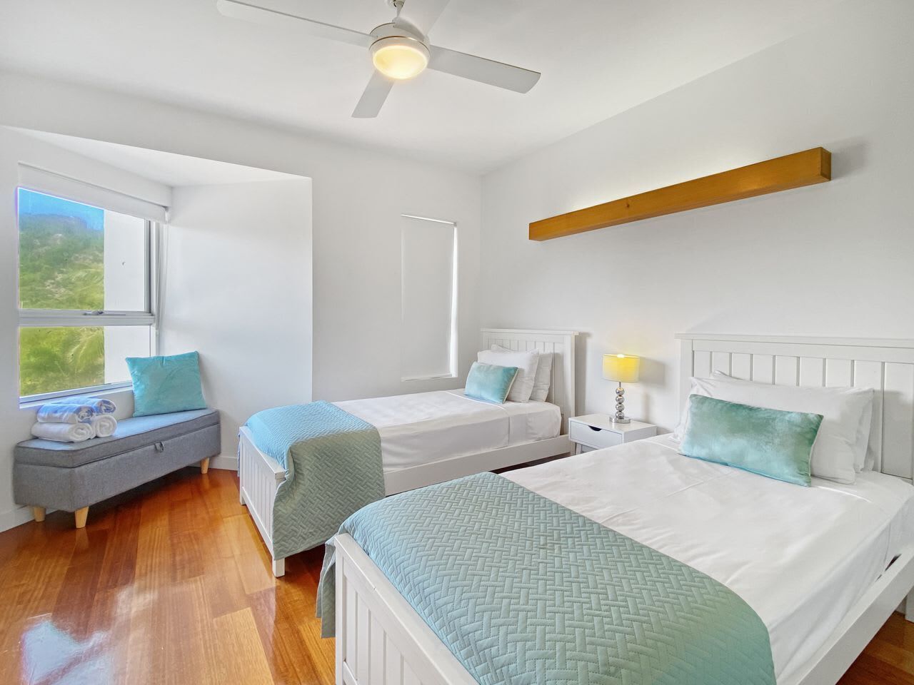 A bedroom with two beds, a bench, a ceiling fan, and a window.