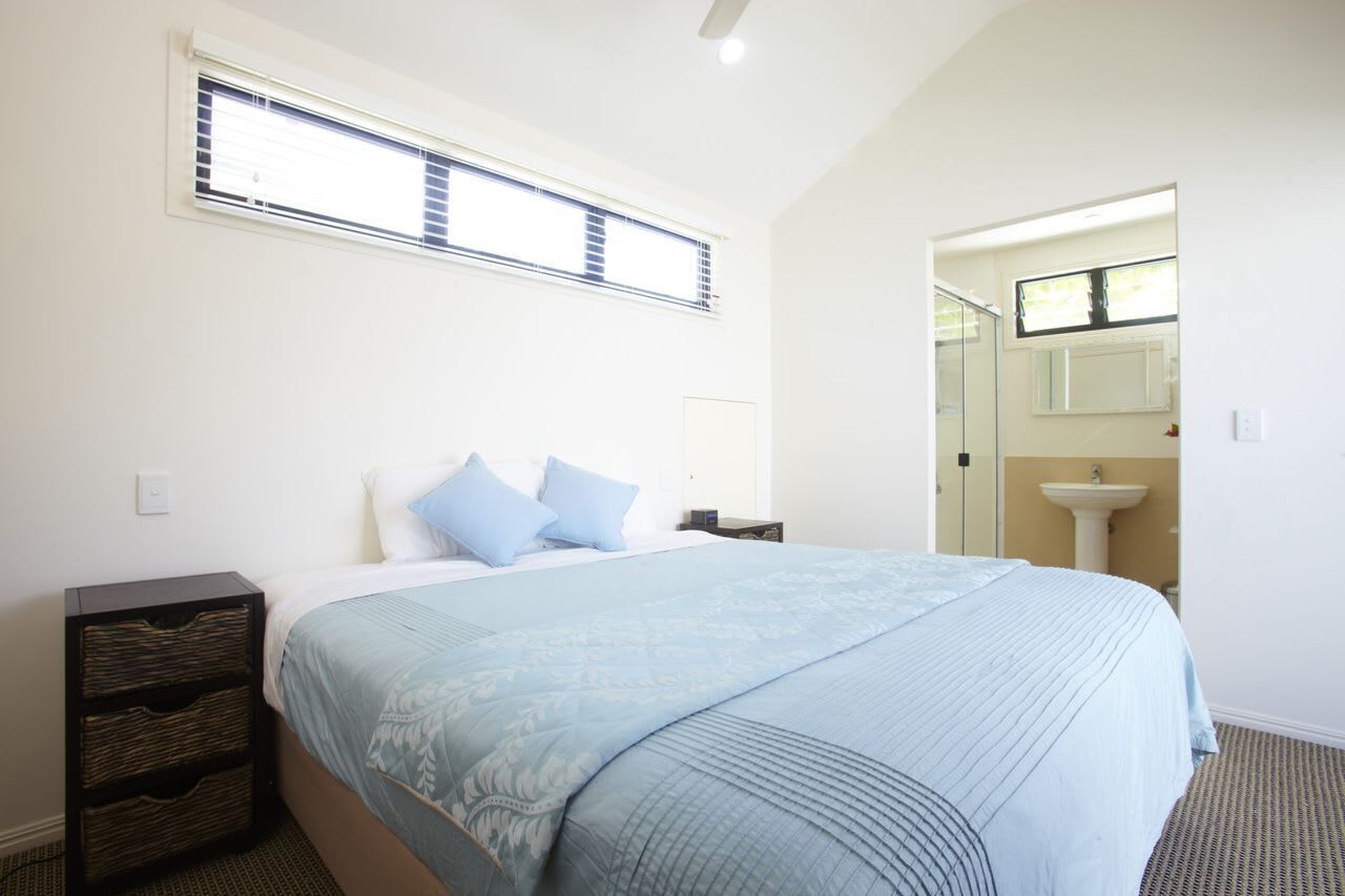 A bedroom with a bed, a nightstand, a window, and a bathroom with a sink and mirror.