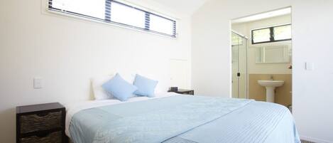 A bedroom with a bed, a nightstand, a window, and a bathroom with a sink and mirror.