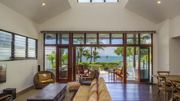 A spacious living room with a large sliding glass door leading to a balcony with a view of the ocean. - Beached on Magnetic (Picnic Bay)
