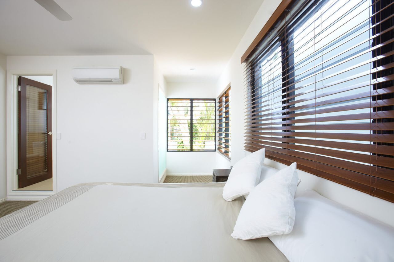 Une chambre moderne avec un grand lit, des stores en bois et une vue sur l’extérieur.