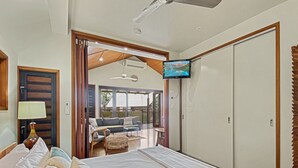 A bedroom with a bed, a TV, a ceiling fan, and a view of the outside.