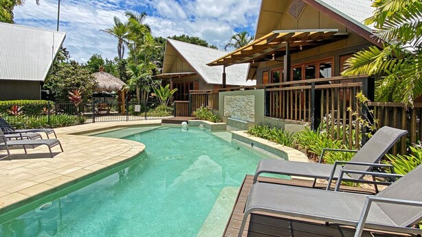 A pool area with lounge chairs, a clear pool, and surrounding tropical vegetation.