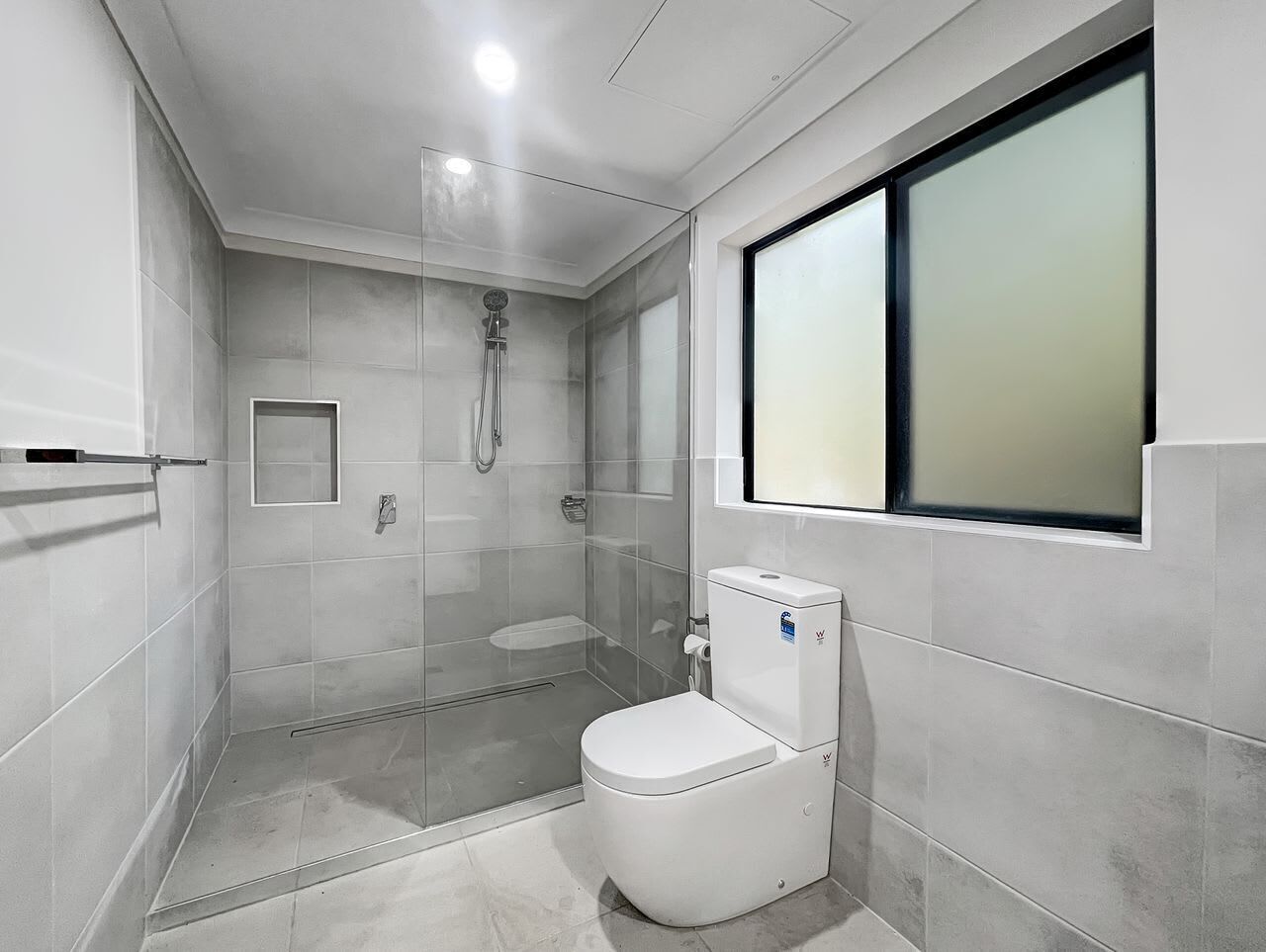 A bathroom with a toilet, a shower, and a window.