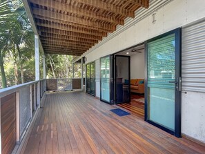 A covered wooden deck with glass doors leading to a room with a sofa and a coffee table. - Deb's Shed (Arcadia)
