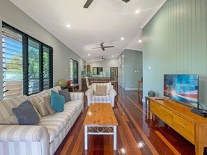 A spacious living area with a sofa set, a coffee table, a TV, and a dining area in the background. - Deb's Shed (Arcadia)