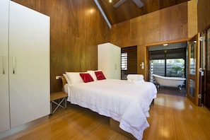 A bedroom with a large bed, a white wardrobe, and a bathtub.