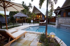 A pool area with lounge chairs, a thatched-roof structure, and a stone wall with a statue. - Pure Magnetic Villa 9 (Nelly Bay)