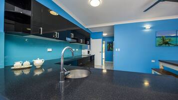 A modern kitchen with a black granite countertop, stainless steel sink, and blue cabinetry.