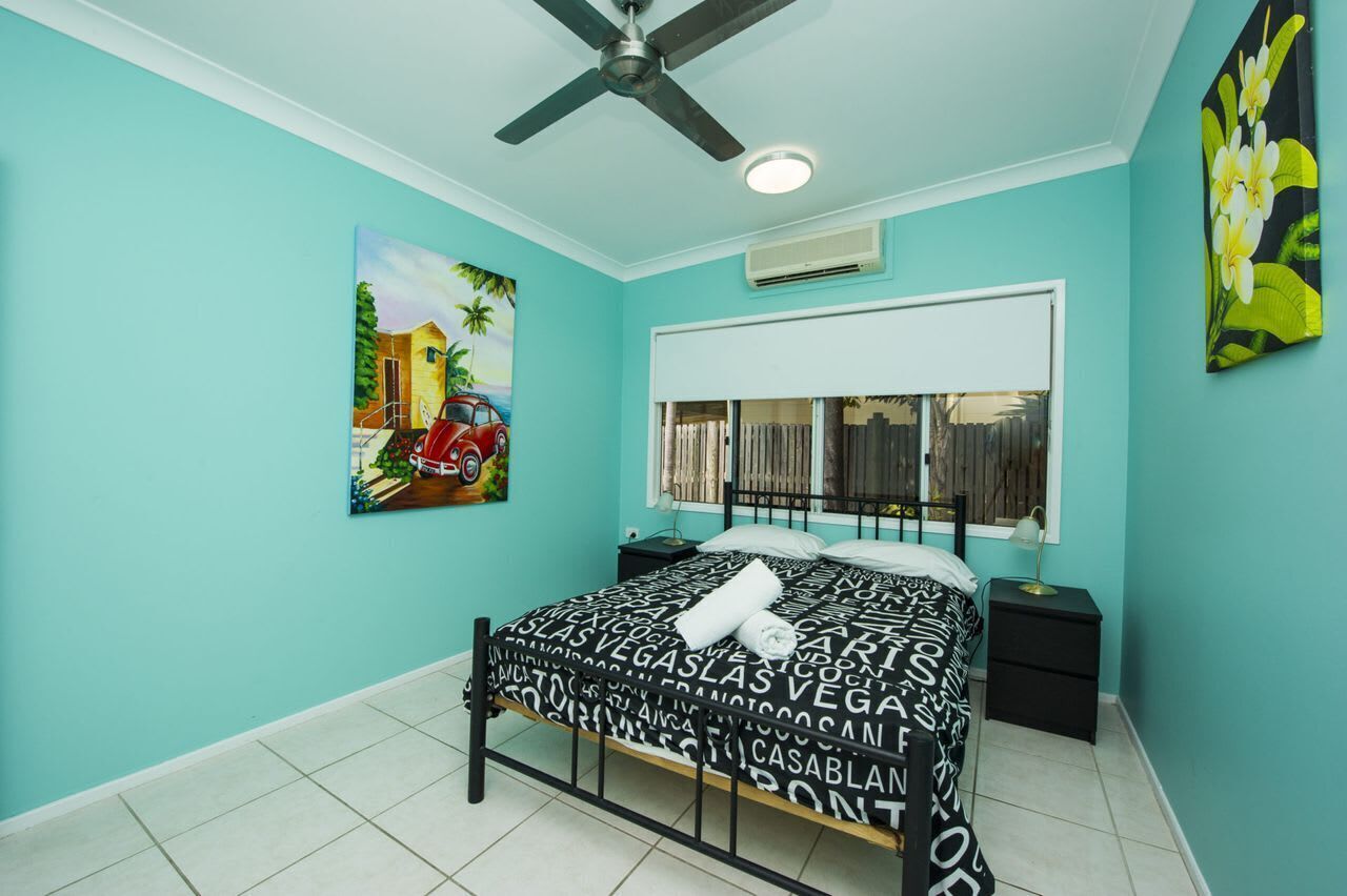 A bedroom with a bed, a ceiling fan, a window with curtains, and wall art.