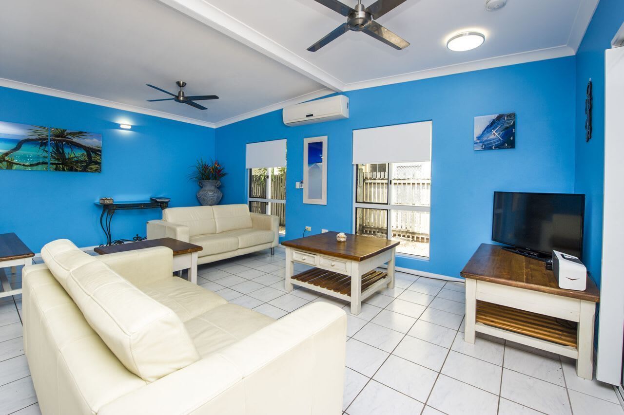 A living room with a sofa, coffee table, TV stand, ceiling fan, and large windows.