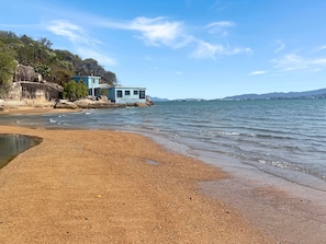 A beach with a house on the shore, a clear sky, and calm water.