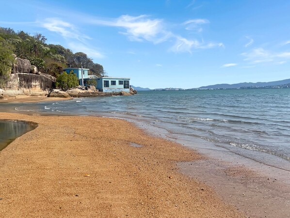 Une plage avec une maison au bord de l’eau, un ciel dégagé et une mer calme.