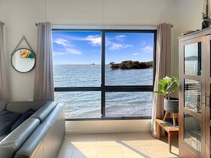 A room with a large window offering a view of the sea, a sofa, a cabinet, and a mirror on the wall. - Blue on Cockle, Cockle Bay-BOM (Cockle Bay)