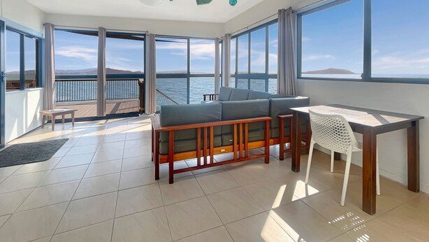 A spacious balcony with a view of the sea, a wooden sofa, a white chair, and a small table. - Blue on Cockle (Cockle Bay)