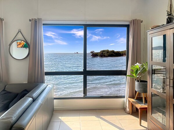 Ein Zimmer mit großem Fenster und Meerblick, einer Couch, einem Schrank und einem Spiegel an der Wand.