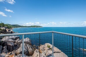 A coastal view with a railing, rocky shoreline, and a distant landmass. - 1 Bright Point Apartment 5404 (Nelly Bay)