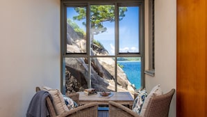 A corner room with a large window overlooking rocky terrain and the sea.