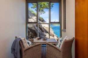 Ein Eckzimmer mit großem Fenster mit Blick auf felsiges Gelände und das Meer.