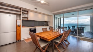A modern kitchen with a dining area, large windows, and a view of the sea.