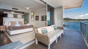 A balcony with a view of the sea, a bedroom with a bed and a sofa, and a shower area.