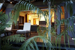 An outdoor seating area with a lounge chair and a table, surrounded by tropical plants. - Pure Magnetic Villa 8 (Nelly Bay)