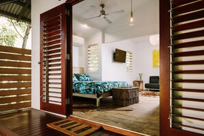 A bedroom with a bed, a ceiling fan, a wall-mounted TV, and a wicker basket. - The Little Bush Hut (Nelly Bay)