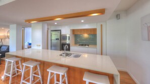 A modern kitchen with a central island, bar stools, a refrigerator, microwave, oven, and a chalkboard backsplash.