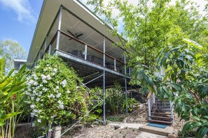 A modern house with a balcony, surrounded by lush greenery and a staircase leading to the upper level.