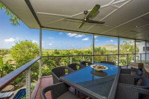 A covered outdoor dining area with a table and chairs, a ceiling fan, and a view of the landscape.