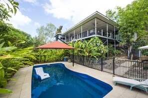 A swimming pool with lounge chairs, a covered patio, and a house with a balcony.