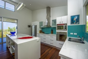 A modern kitchen with white cabinetry, a stainless steel refrigerator, a microwave, and a large window.