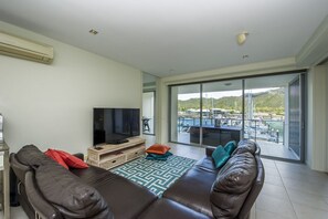 Ein Wohnzimmer mit Sofa, Fernseher und Blick auf Pool und Berge.