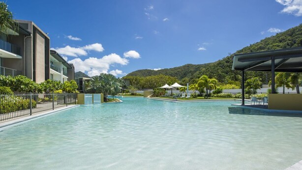 A swimming pool with a clear blue sky, a mountain in the background, and a covered area with chairs.