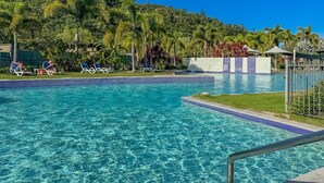 Piscina cristalina con azulejos azules, rodeada de sillas de descanso y una zona verde.