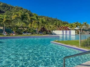 A clear swimming pool with blue tiles, surrounded by lounge chairs and a grassy area. - Blue on Blue Apartment 1011 (Nelly Bay)