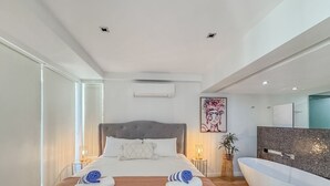 Un dormitorio moderno con una cama grande, una bañera integrada y un espejo amplio.